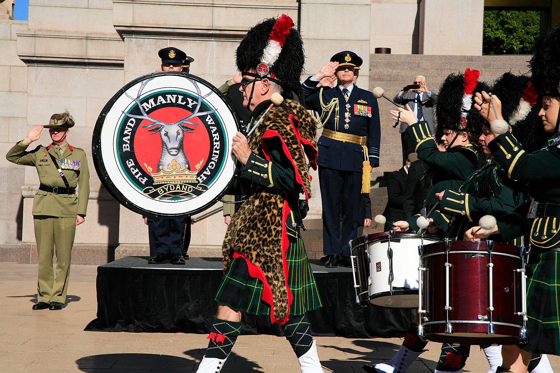 A marching band parades across the Memorial' northern forecourt. Defence Personnel salute as they pass.