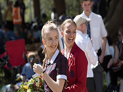 Two female secondary school students carrying a floral wreath glancing back over their left shoulders
