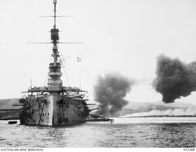 HMS Cornwallis, the last ship to leave the Anzac Cove area after the evacuation conducted on the night of 19-20 December 1915. Here she is shown replying to Turkish artillery firing from inland. Note the burning piles of stores on the beach in the background. Courtesy AWM