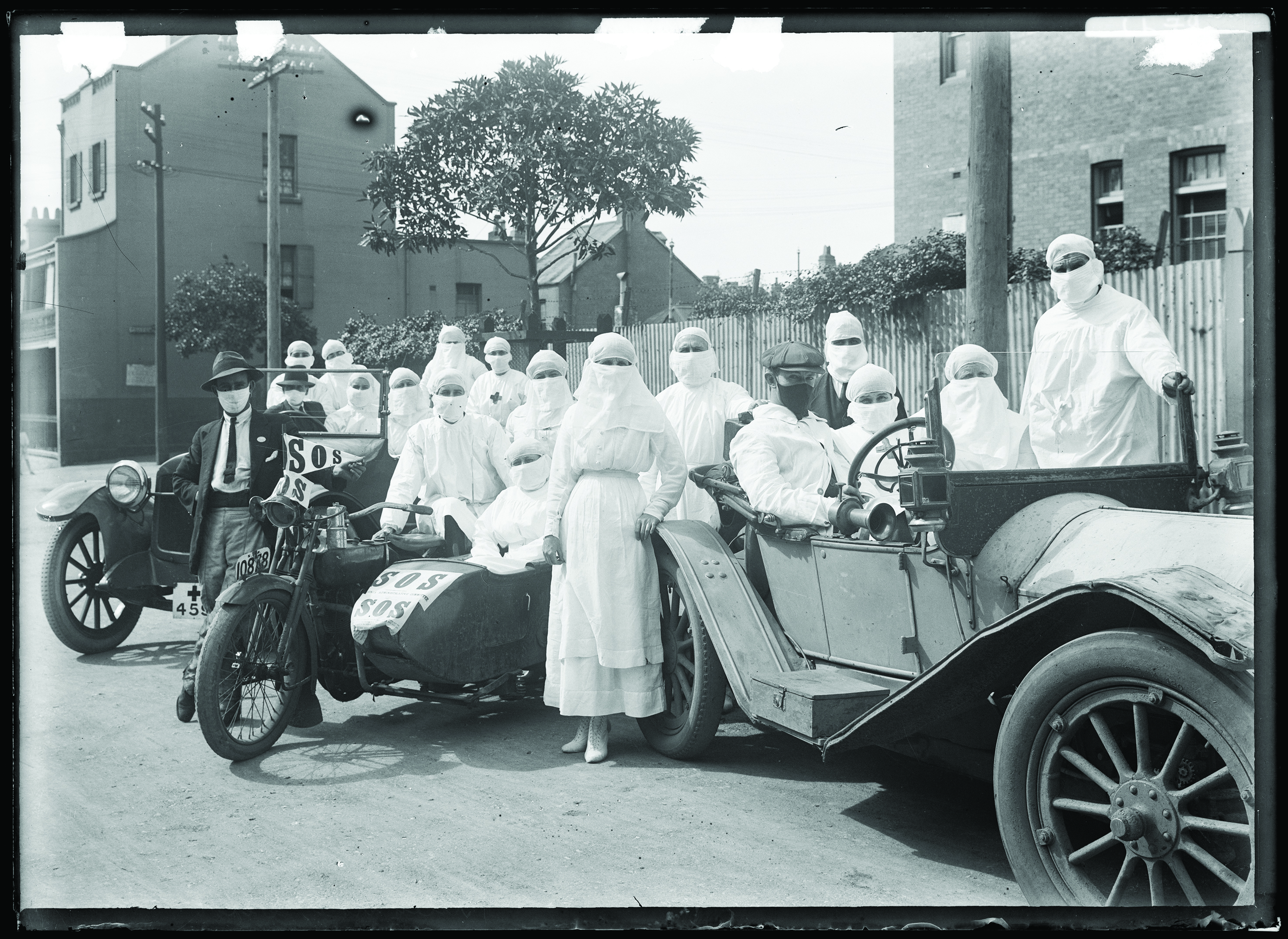 A group of nurses and doctors dressed in surgical whites and masks about to get on motorbikes and cars to tend influenza patients