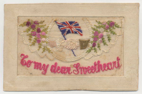 Embroidered silk postcard with flowers and clasped male and female hand in front of Union Jack on the top and the phrase 'To my dear sweetheart' on the bottom. These cards were incredibly popular with members of the AIF who regularly sent them home to female relatives and loved ones. AWM RC04566.003.