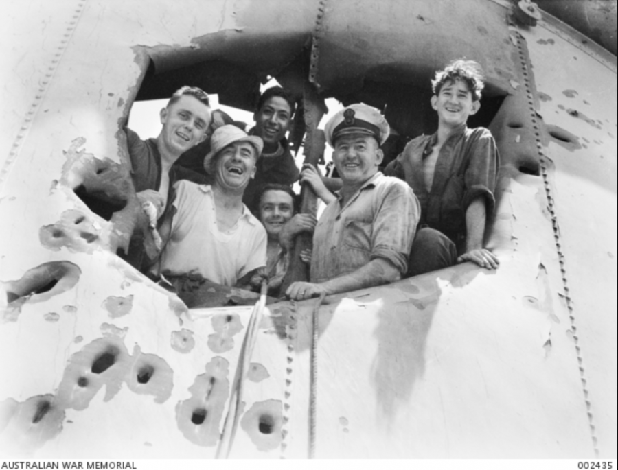 Crew members of HMAS 'Sydney' peer through a hole in the forward funnel. The damage was sustained in action against the Italian Cruiser 'Bartolomeo Colleoni' off Cape Spada, Crete. AWM 002435.