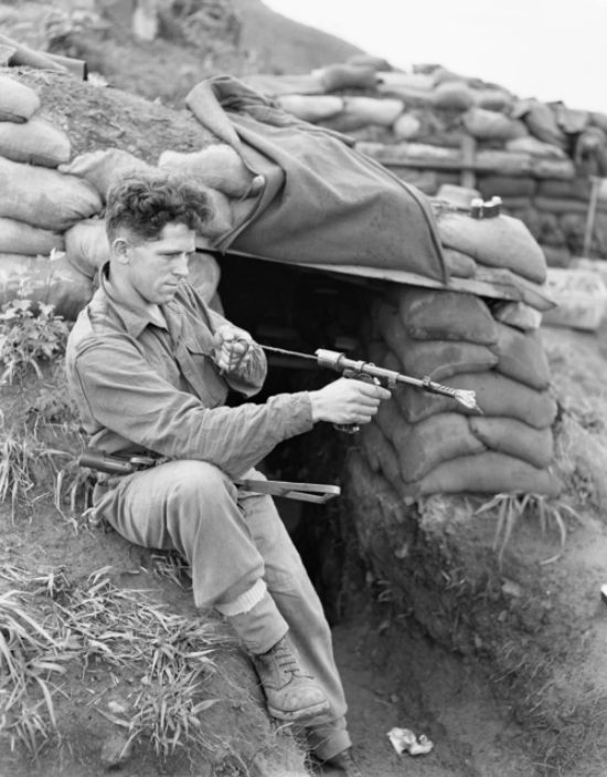 Private Eddie Wright cleans his Owen gun outside his hutchi on the Jamestown Line, Korea, 14 May 1953. AWM HOBJ4260.