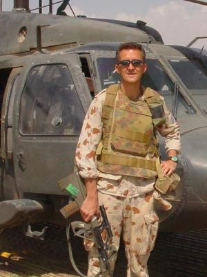 Tony standing in front of a helicopter in his army fatigues with a rifle